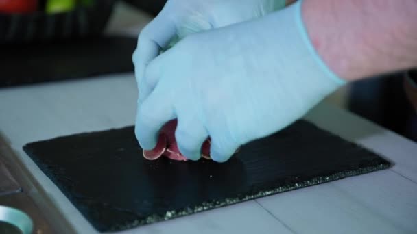 Готувати в рукавичках розкладає нарізаний джемон або м'ясо на чорній тарілці на кухні ресторану, їжа — стокове відео