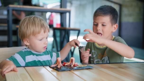 Kinderen voedsel, schattig klein hongerig mannelijk kind met een eetlust eten gezond ontbijt gegrilde worsten en eieren met groenten in cafe — Stockvideo