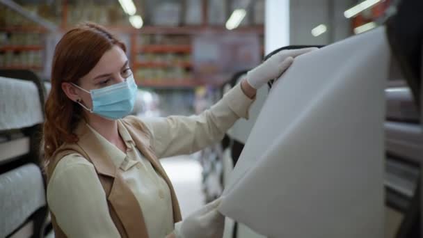 Naprawy koronawirusa, młoda kobieta w masce i rękawiczkach wybiera tapetę w sklepie z narzędziami podczas izolacji i pandemii — Wideo stockowe