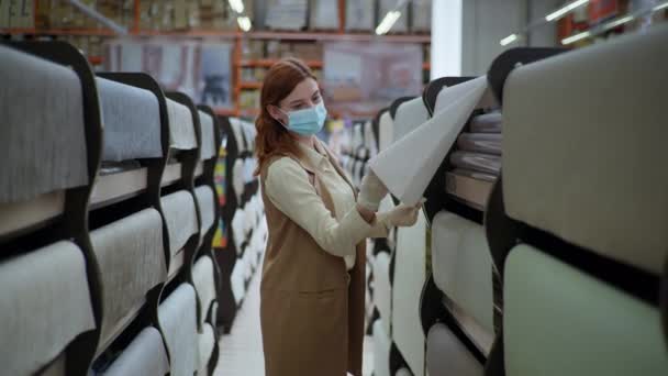 Entretenimiento cuarentena, cliente femenino en máscara médica y guantes elige nuevo fondo de pantalla para las reparaciones en el apartamento — Vídeo de stock