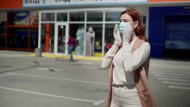 Ung kvinnelig shopper tar på seg medisinsk maske og hansker for å beskytte mot farlig dødelig virus foran inngangen til supermarkedet – stockvideo