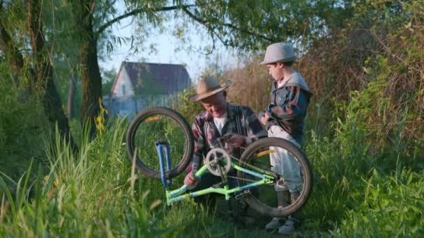 Vztah s dětmi, pečlivý domácnost pohledný starý muž se svým pěkným vnoučátkem v kloboucích kontroluje pedály a kola na kole při chůzi podél břehu řeky — Stock video