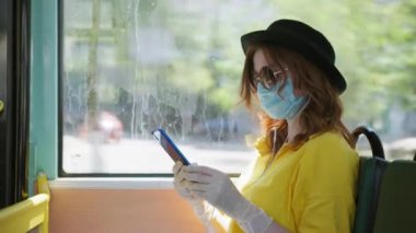 Virüs ve enfeksiyondan korunmak için tıbbi maske ve eldiven takan kadın yolcular şehir otobüsleri sırasında cep telefonlarından müzik dinliyorlar.