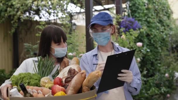 Entrega de alimentos, jovem mensageiro feminino atraente vestindo máscara médica e luvas para proteger contra vírus e infecção entrega comida meninas para sua casa — Vídeo de Stock