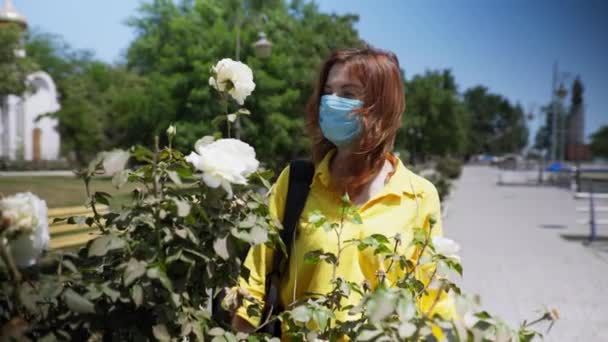 아름다운 소녀는 세계적 유행병이 발생하는 동안 안전 대책을 관찰하고 의학적 보호 마스크를 쓰고 꽃 냄새를 맡기 위해 인공호흡기를 벗는다 — 비디오