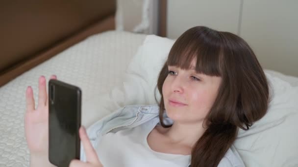 Online winkel, vrolijke meisje bestelt boodschappen via internet en moderne app in de supermarkt met thuisbezorging terwijl ontspannen thuis op bed tijdens isolatie en pandemie — Stockvideo