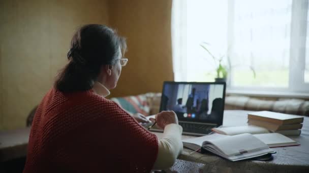 Κατάρτιση σε απευθείας σύνδεση, ηλικιωμένη γυναίκα σπουδάζει σε απευθείας σύνδεση με τη βοήθεια των σύγχρονων τεχνολογιών που κάθονται στο σπίτι από ένα τραπέζι με έναν φορητό υπολογιστή — Αρχείο Βίντεο