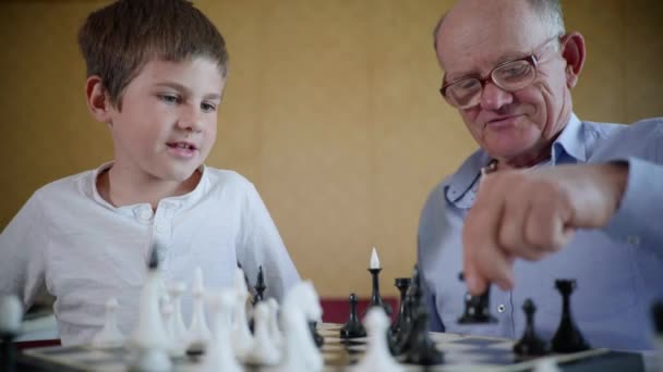 Gyermek fejlődés, vidám nagyapa szemüveggel a látvány és a boldog unoka mosolyognak és sakkoznak — Stock videók