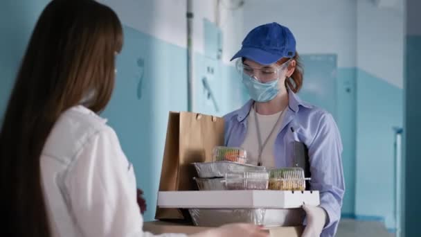 Pandemi, ung flicka i medicinsk mask beställer mat av kvinnliga kurir bär respirator och handskar under karantän på självisolering — Stockvideo