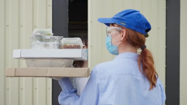 Conceito de compras on-line, empregado da loja de entrega da mulher vestindo uma máscara médica protetora traz comida para um jovem cliente em casa durante o auto-isolamento e quarentena — Vídeo de Stock