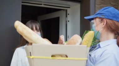 Teslimat servisi, kadın kurye güvenlik kurallarına uyarak koruyucu maske eldivenleri takıyor, gözlük, salgın sırasında karantinaya alınan genç bir kadına çevrimiçi dükkandan yiyecek getiriyor.