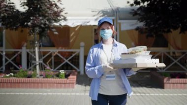Genç kız kurye güvenlik önlemlerini gözlemliyor. Virüse karşı eldiven ve gözlük takan tıbbi maske ve gıda dağıtım restoranlarında işe yarıyor.