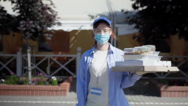 Μέτρα υγιεινής ασφαλείας, νεαρή κοπέλα courier τηρεί προφυλάξεις ασφαλείας ιατρική μάσκα με γάντια και γυαλιά κατά του ιού και της μόλυνσης έργα στο εστιατόριο παράδοσης τροφίμων κρατά κουτιά πίτσα χαμογελώντας — Αρχείο Βίντεο