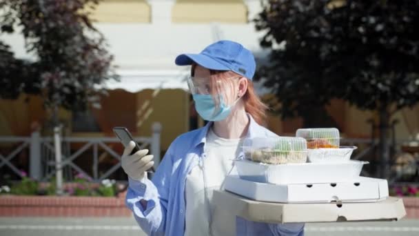 Karantän leverans service, kvinnliga kurir bär medicinsk mask, skyddsglasögon och handskar för att skydda mot virus och infektion med pizza lådor i handen tittar på smartphone matleveransadress — Stockvideo