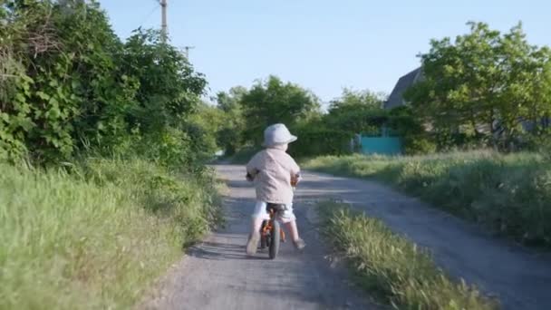 Feliz infancia, pequeño chico guapo en sombrero de paja tiene divertido ciclismo mientras se relaja fuera de la ciudad en las vacaciones de verano — Vídeos de Stock