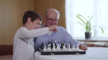 Çocuklarla ilişki, gözlüklü yaşlı sempatik büyükbaba akıllı küçük torun eğitim tahtası satranç oyunlarıyla oynuyor.
