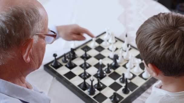 Frühkindliche Entwicklung, ein kleines intelligentes männliches Kind spielt mit seinem liebenden Großvater Brettspiele im Schach — Stockvideo