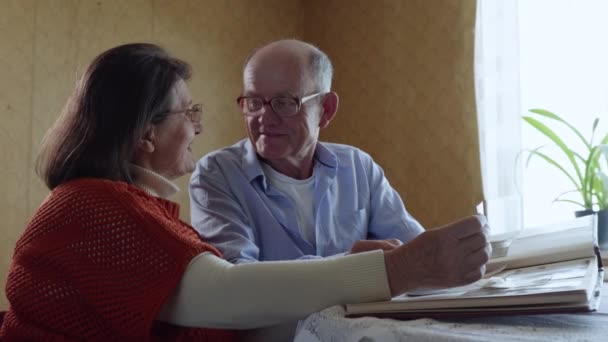 Gelukkige herinneringen, een liefhebbende oudere man geniet van het gezinsleven kust zijn geliefde vrolijke oudere vrouw tijdens het kijken naar een fotoalbum — Stockvideo