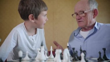 Aile eğlencesi, sempatik neşeli çocuk yaşlı büyükbabasıyla gözlüklü satranç tahtası oyunu için oynuyor.