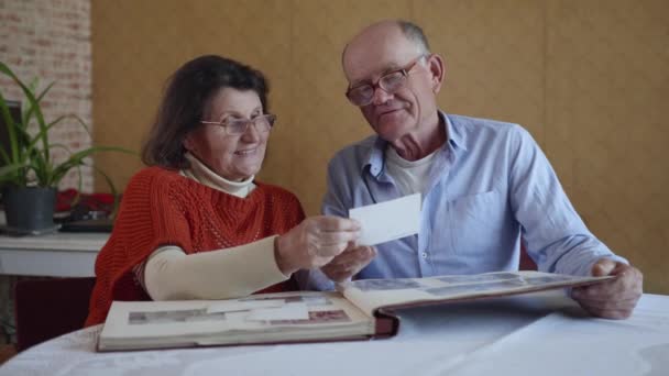 Úspěšné manželství, starší manžel a žena, kteří si zachovali lásku a péči o sebe navzájem, jsou inspirováni vzpomínkou na roky, které prožívali v rodinném fotoalbu — Stock video