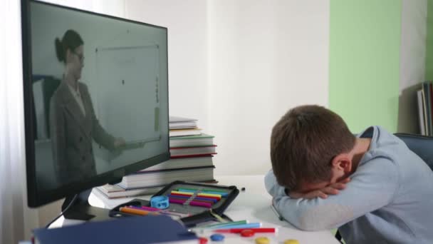 Niño estudiante de escuela primaria sufre de aprendizaje en línea no entiende las explicaciones de los profesores puso la cabeza en sus manos mientras estaba sentado en la mesa — Vídeo de stock