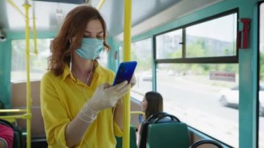Tıbbi maske takan ve eldiven takan genç bir kız karantina sonrası şehirde dolaşırken akıllı telefonuyla müzik dinliyor.