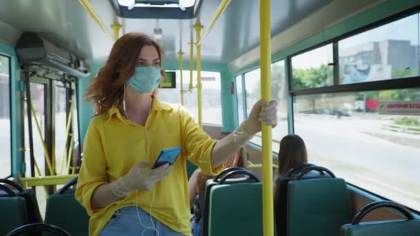 Pandemický výlet, dívka cestující v lékařské masce a rukavice jízdy v městském autobuse, poslech hudby na sluchátka po zrušení karantény — Stock video