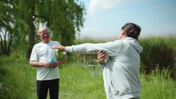 Eldre kvinner leder sporty livsstil og utfører håndverksøvelser fra ektemanns leddsmerter under trening utendørs – stockvideo