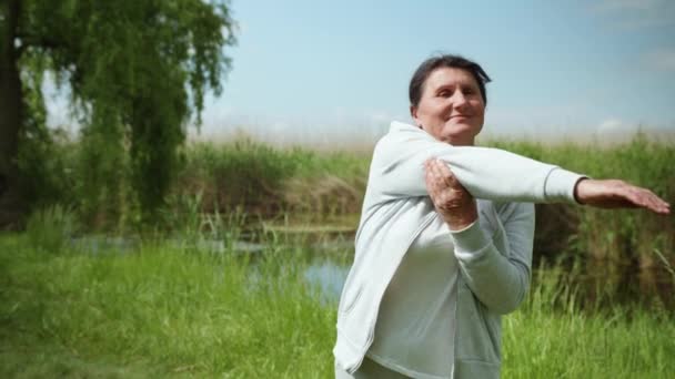 Счастливая пожилая женщина ведет здоровый образ жизни идет в спорте делает упражнения для рук — стоковое видео