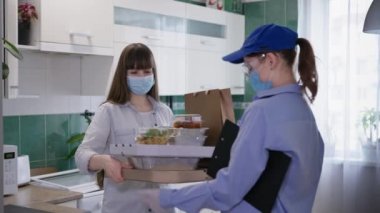 Kilit altında, tıbbi maske ve eldiven takan kadın kurye karantina ve sosyal izolasyon sırasında solunum cihazı takan genç kıza yiyecek getiriyor.