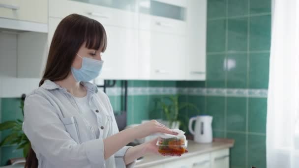 Zpracování potravin, dospělá dívka v lékařské masce dodržuje opatření a dezinfikuje nádoby s jídlem, které kurýr zanechal doma během pandemie viru a infekce — Stock video