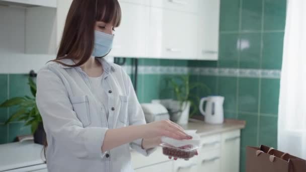 Säkerhetshygien åtgärder, ung hemmafru bär skyddande medicinsk mask servetter behållare livsmedel levereras med kurir från en antiseptisk produkt under coronavirus pandemi — Stockvideo
