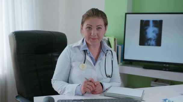 İnternet 'te, güzel doktor kadın modern teknolojiyi kullanarak hastaya danışmanlık yapıyor ve masada oturan röntgen cihazını kullanarak hastalık belirtilerini açıklıyor. — Stok video