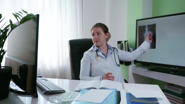 Медицинское обслуживание, женщина-врач консультируется с онлайновым пациентом, рассказывая симптомы заболевания с помощью рентгеновского снимка, используя видео-ссылку на компьютере и веб-камеру — стоковое видео