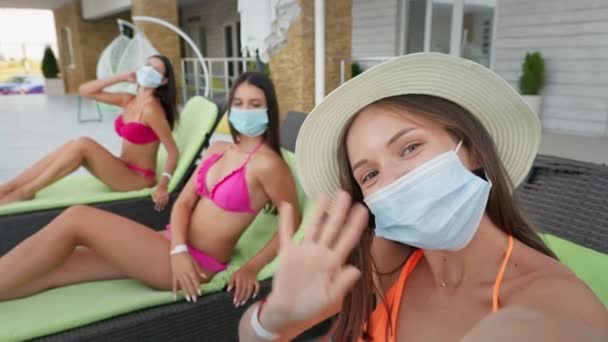 Cuarentena selfie verano, alegres novias jóvenes con máscaras médicas protectoras observan las reglas de seguridad mientras se relaja en las tumbonas con teléfono inteligente — Vídeo de stock