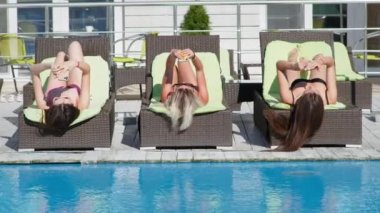 Mayolu çekici genç kızlar sıcak bir günde güneşlenirken akıllı telefonlarını kullanırlar.