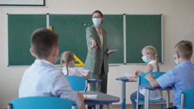 Maskeli okul çocuğunun portresi öğretmen sorusunu cevaplıyor. Sonra da bir ders sırasında başparmağını masaya oturturken kameraya çeviriyor.