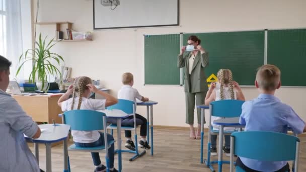 CVID 이후의 새로운 정상적 인 삶, 칠판 가까이에 있는 여성 교사는 교실에서 수업중에 의학용 마스크를 쓰는 방법을 보여 줍니다. — 비디오