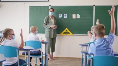 Salgın sırasında ders çalışmak, tıp maskeli bir öğretmen ve beyaz tahtaya yakın bir yerde gözlük takmak öğrencilere sorular sormak, liseli kız cevap vermeye ve elini kaldırmaya hazır.