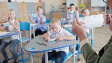Yeni normallik, okul çocukları öğretmene bakıyorlar ve maske takıyorlar okulda maske takıyorlar.