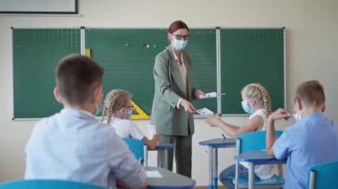 Karantinadan sonra okulda çalışmak, öğretmenlerin ders sırasında çocuklara ödev broşürleri dağıtması, maskeli öğrencilerin kameraya bakıp başparmaklarını kaldırması.