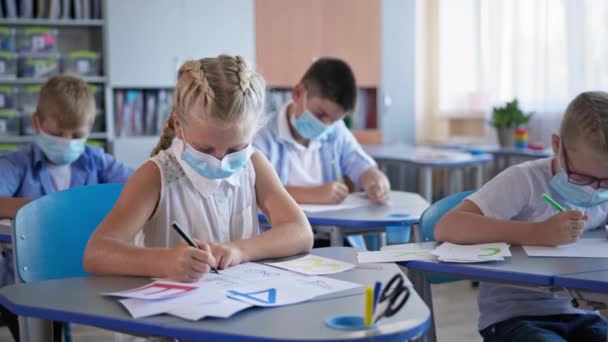 Portret van schoolmeisje met medisch masker dat klaswerk doet aan het bureau, leerlingen terug op school na covid-19 quarantaine en lockdown — Stockvideo