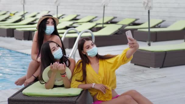 Vacanza coronavirus, giovani donne indossano maschere mediche protettive durante la distanza sociale prendendo selfie in piscina durante le vacanze estive al resort — Video Stock