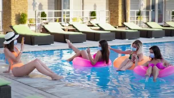 Rust tijdens coronavirus infectie, vriendinnen met maskers foto 's maken op mobiele telefoon en ontspannen in het zwembad in de zomer — Stockvideo
