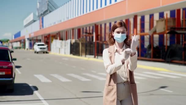 Pandemia, młoda piękna dziewczyna w rękawiczkach i maskach w celu ochrony przed wirusami, zakażeniami lub chorobami w pobliżu centrum handlowego przestrzega środków bezpieczeństwa podczas koronawirusu — Wideo stockowe