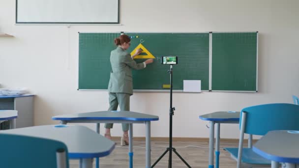 Pedagogo com régua na mão perto de quadro-negro usando câmera de vídeo celular gravando-se no ensino de matemática on-line na escola, para evitar a infecção por coronavírus durante o social — Vídeo de Stock