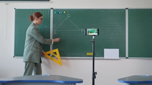 Kształcenie na odległość dla uczniów, młody nowoczesny nauczyciel w pobliżu tablicy prowadzi lekcje matematyki online dla uczniów korzystających ze smartfona podczas kwarantanny — Wideo stockowe