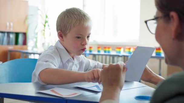 Life with disabilities, boy with downs syndrome studying mathematics with teacher sitting at desk in classroom at elementary school — Stock Video