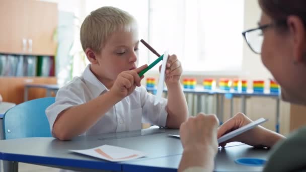 Criança com síndrome de Down na escola, aluno com deficiência estudando matemática com a professora sentada na mesa em sala de aula — Vídeo de Stock
