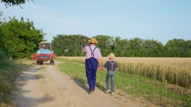 Agrobyznys, starší farmář kráčí ruku v ruce se svým vnukem — Stock video